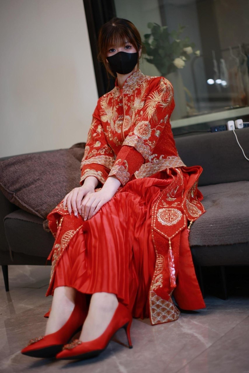 白龙猫女戴黑色口罩身着红金刺绣中式婚服坐在灰色沙发旁 白龙猫女戴黑色口罩身着红金刺绣中式婚服坐在灰色沙发旁