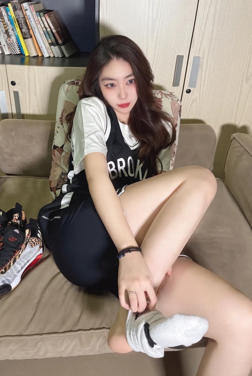 杨晚柠穿黑白球衣在浅木书柜前坐拍并整理白色短袜