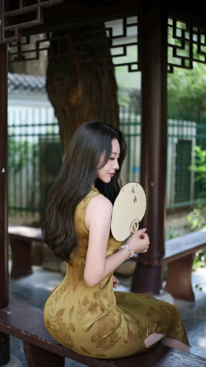 杨晚柠穿金黄色花纹旗袍手持团扇坐在木格亭廊内