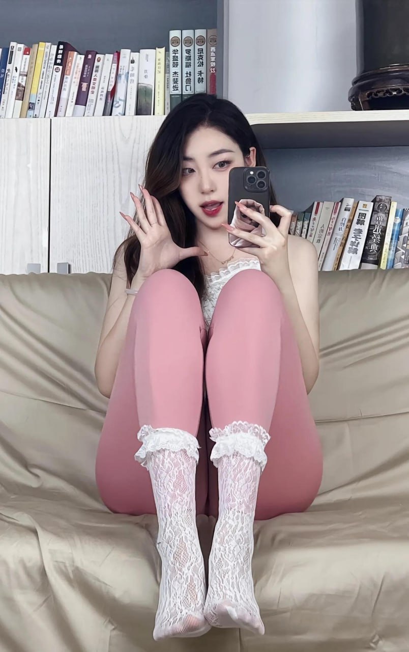 杨晚柠穿粉色长裤与白色上衣在书柜前手持黑色手机
